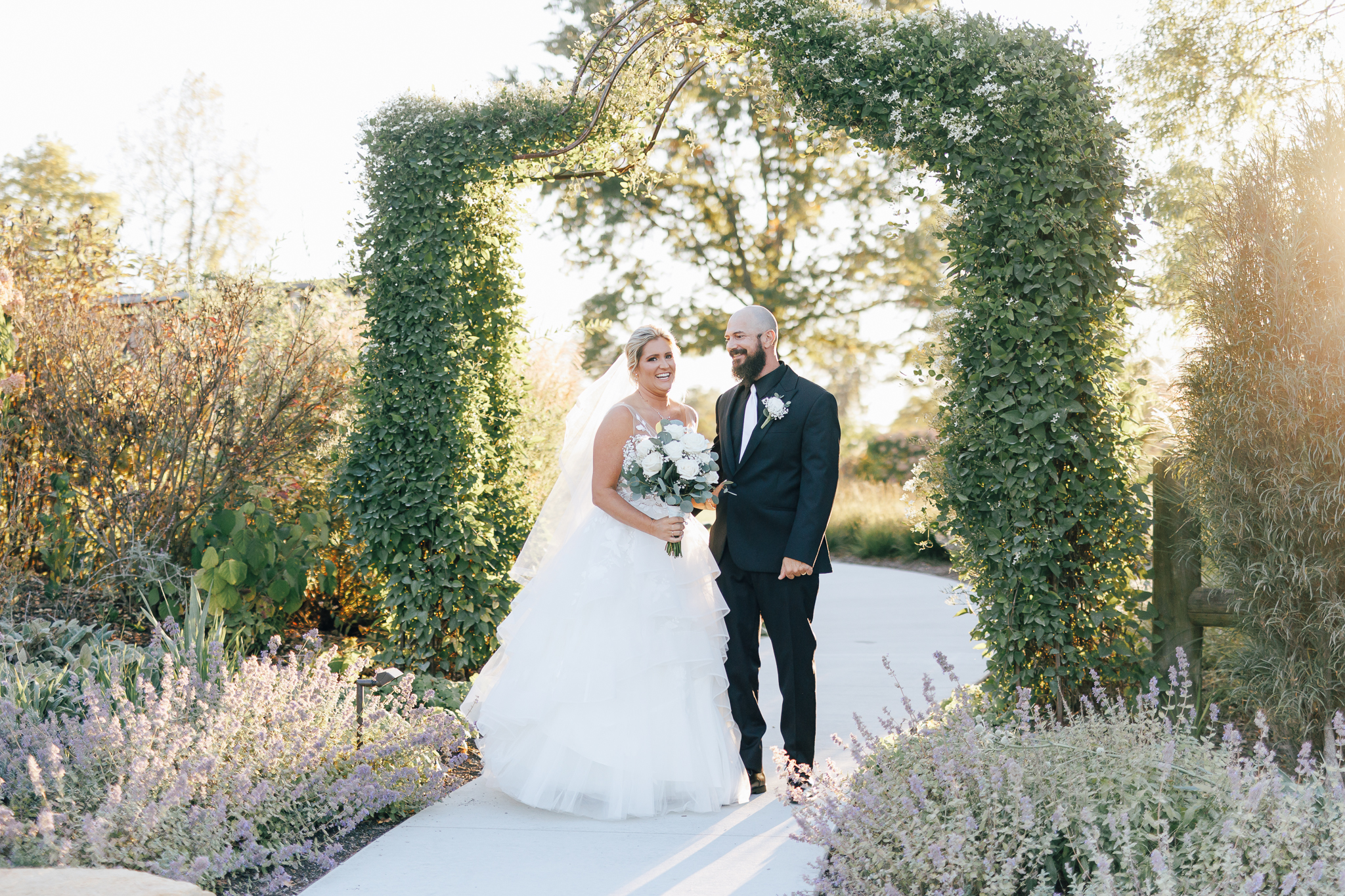 bride and groom stand infront of full greenery arch