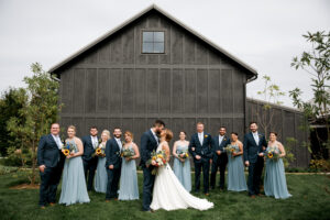 Wedding party wearing blue infront of black barn at Jorgensen Farms wedding venue