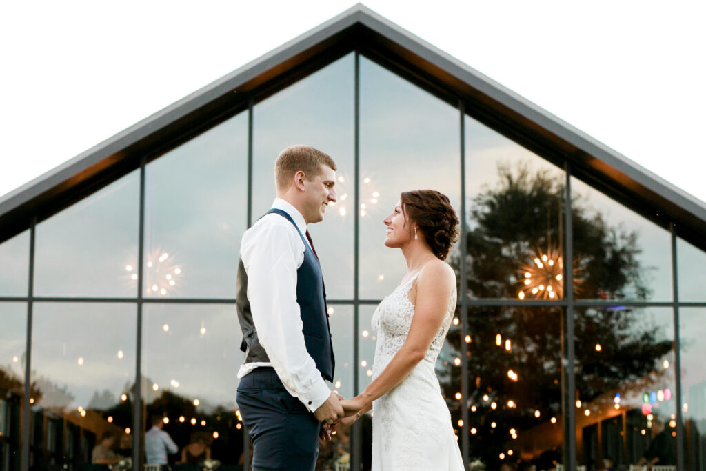 wedding couple poses infront of glass wall of windows at wedding venue in Columbus oh