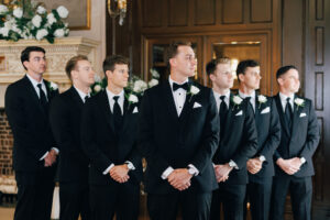 groomsmen and groom standing in v shape looking left in black tuxes