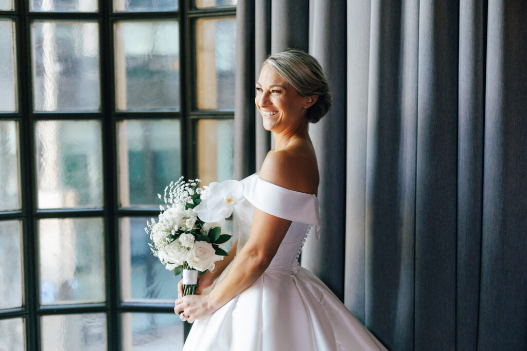 bride holding bouquet and standing infront of blue curtain window at the athletic club wedding venue