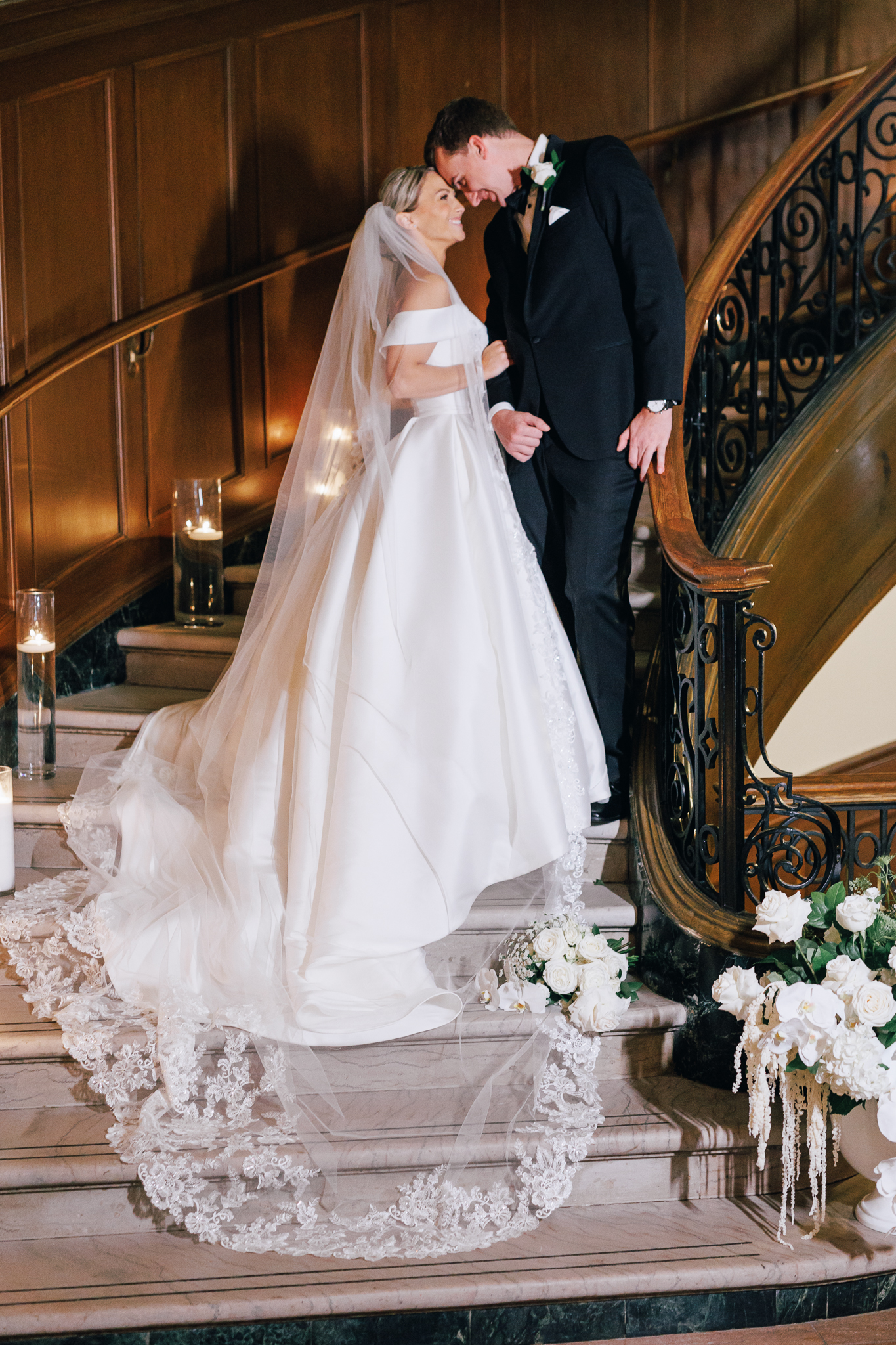 bride and groom kissing on spiral staircase with wooden paneling and candles and florals on steps