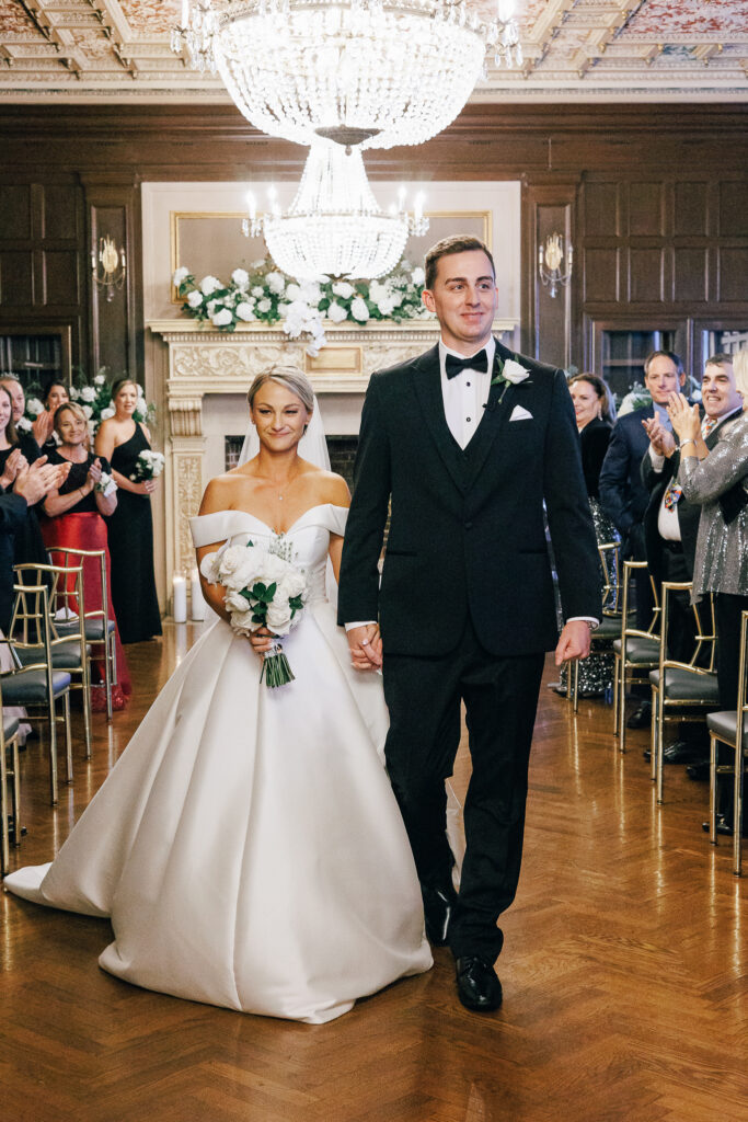 Bride and groom walk down the aisle after getting married infront of glamorous fireplace