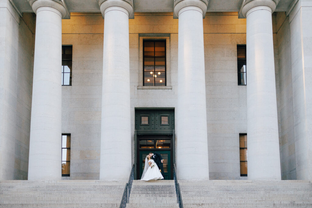 bride and groom kiss infront of marble pillars and staircase