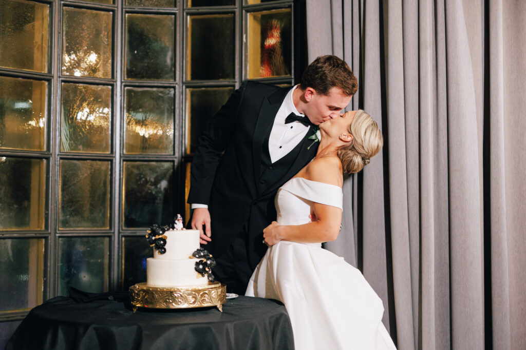 bride and groom kissing after cutting wedding cake at the athletic club wedding venue