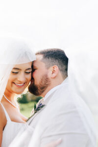 bride and groom with veil tossed over their heads telling a secret