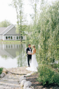 bride and groom stand infront of weeping willow near pond