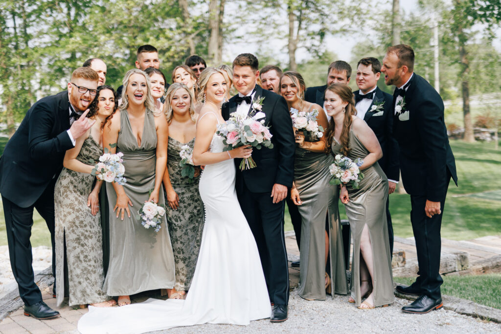 bride and groom stand with large bridal party wearing green bridesmaid dresses