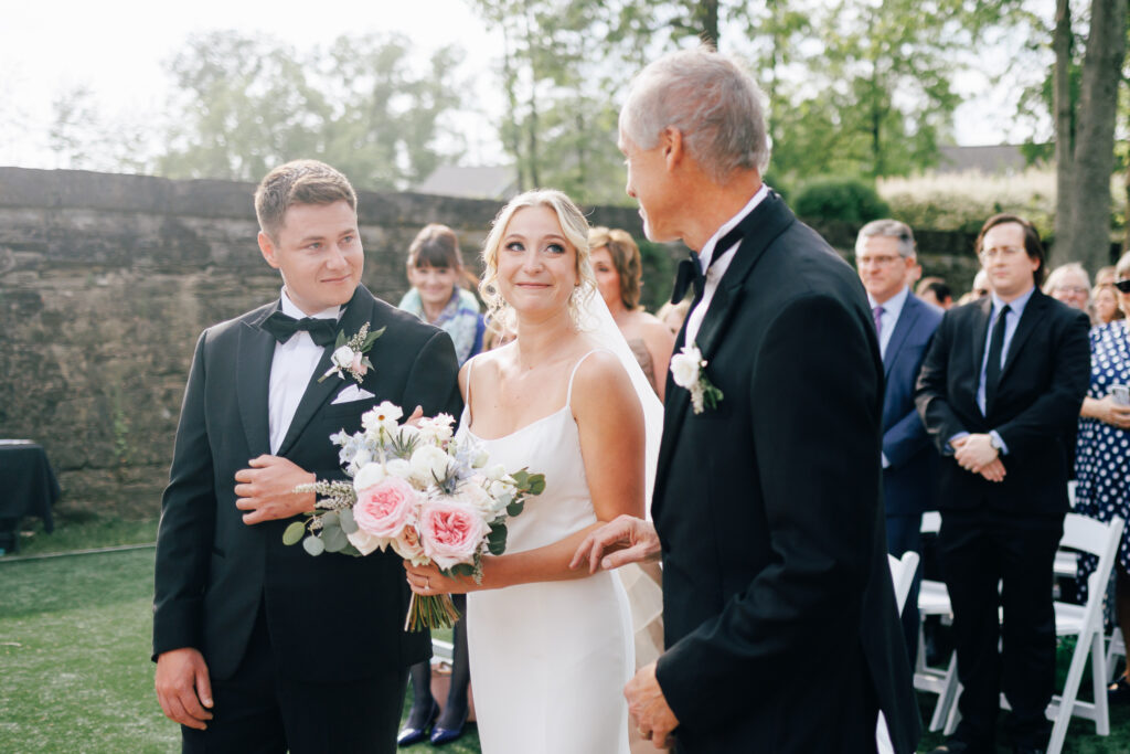 bride looks at father as she grabs grooms arm at a wedding