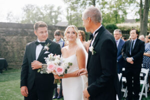 bride looks at father as she grabs grooms arm at a wedding