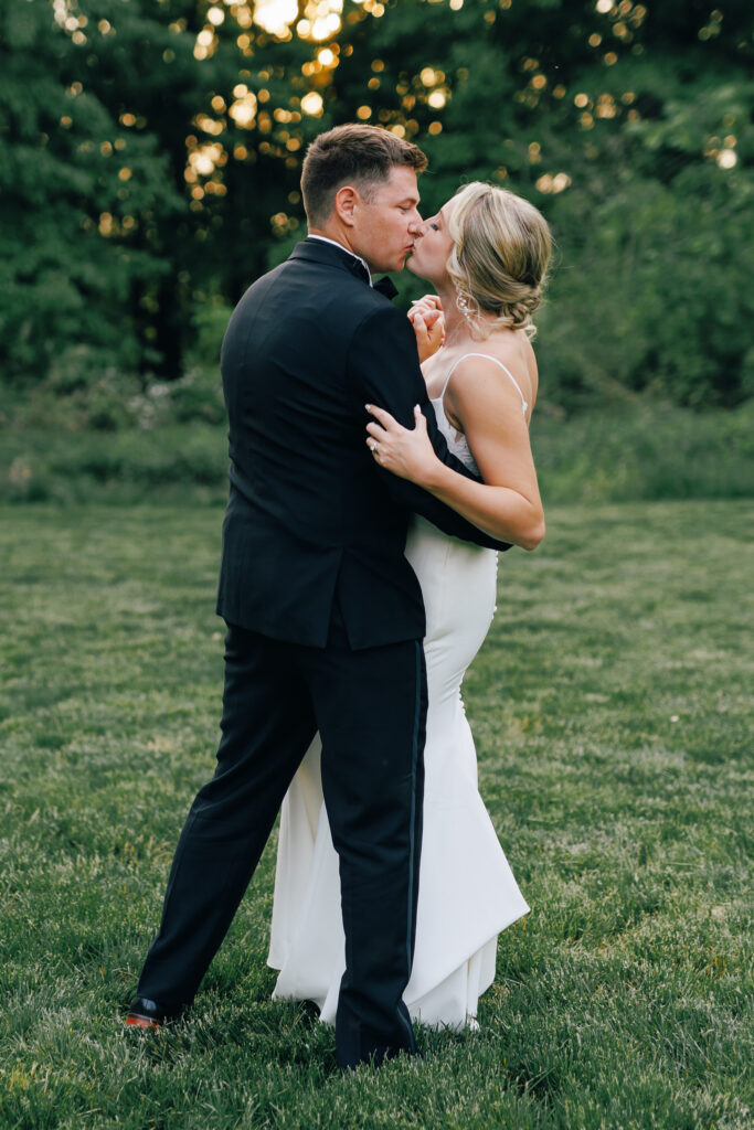 bride and groom kiss in grassy field