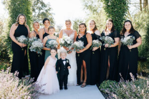 bridesmaids wearing black gowns surrounding bride for bridal party portriat in garden at Jorgensen Farms