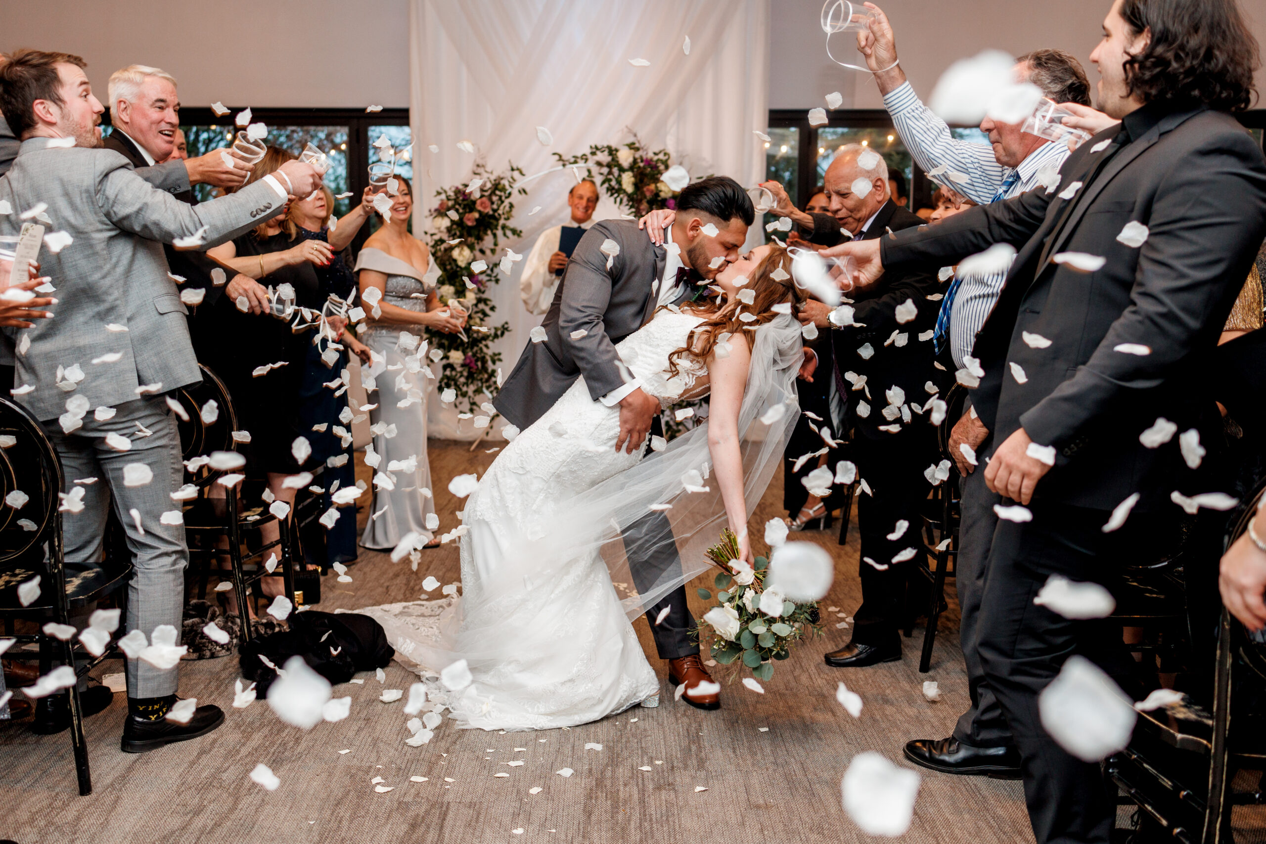 bride and groom kissing at the aisle of thier wedding as guests throw petals at Brookshire Events Center