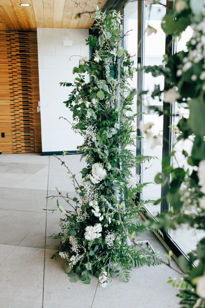 floral wedding arch with white roses and greenery infront of wooden wall and floor length windows at the rooftop of The Fives wedding venue in Columbus Ohio