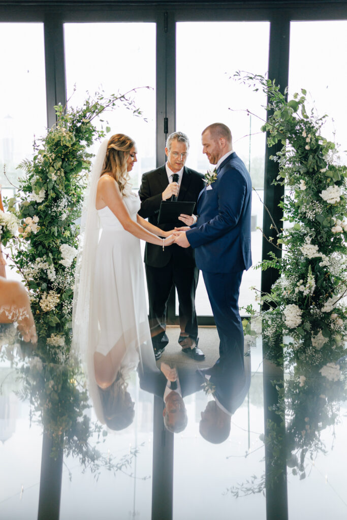 Bride and groom stand infront of full length windows and floral round arch to say thier vows at The Fives Wedding venue in Columbus Ohio