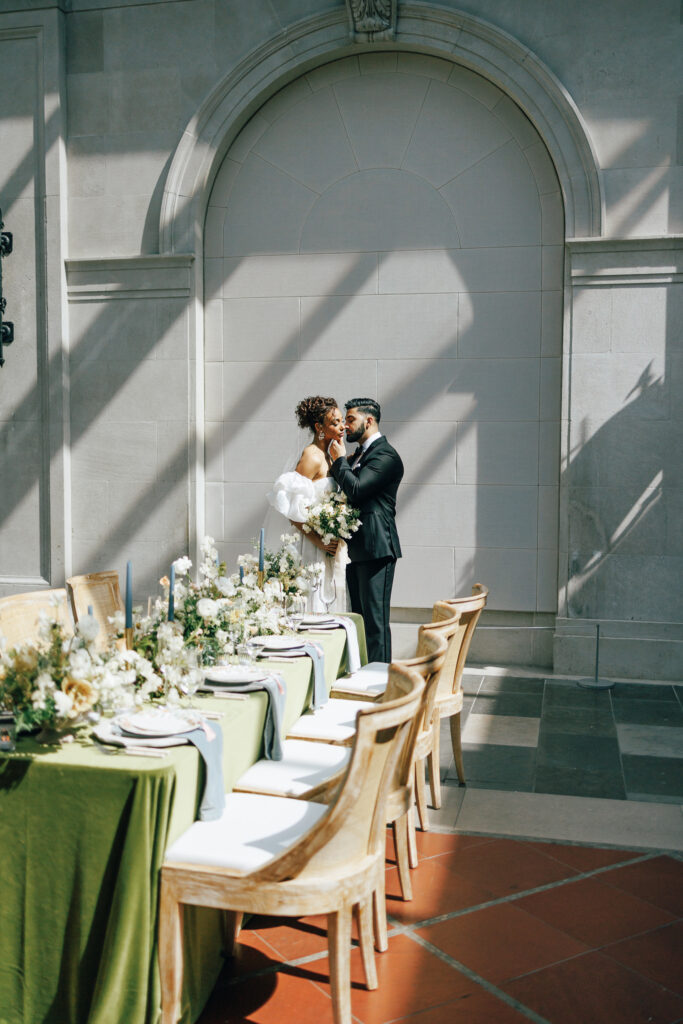 bride and groom kissing against marble arch in front of styled table at the Columbus Museum of Art wedding veneu