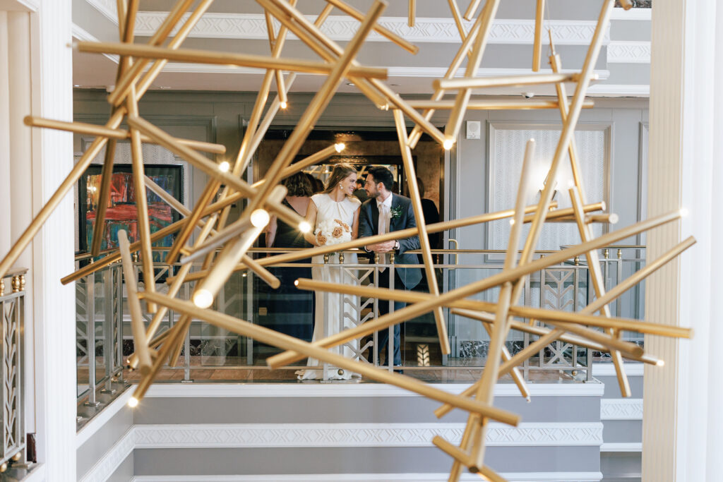 bride and groom stand infront of modern gold chandelier at le veque hotel