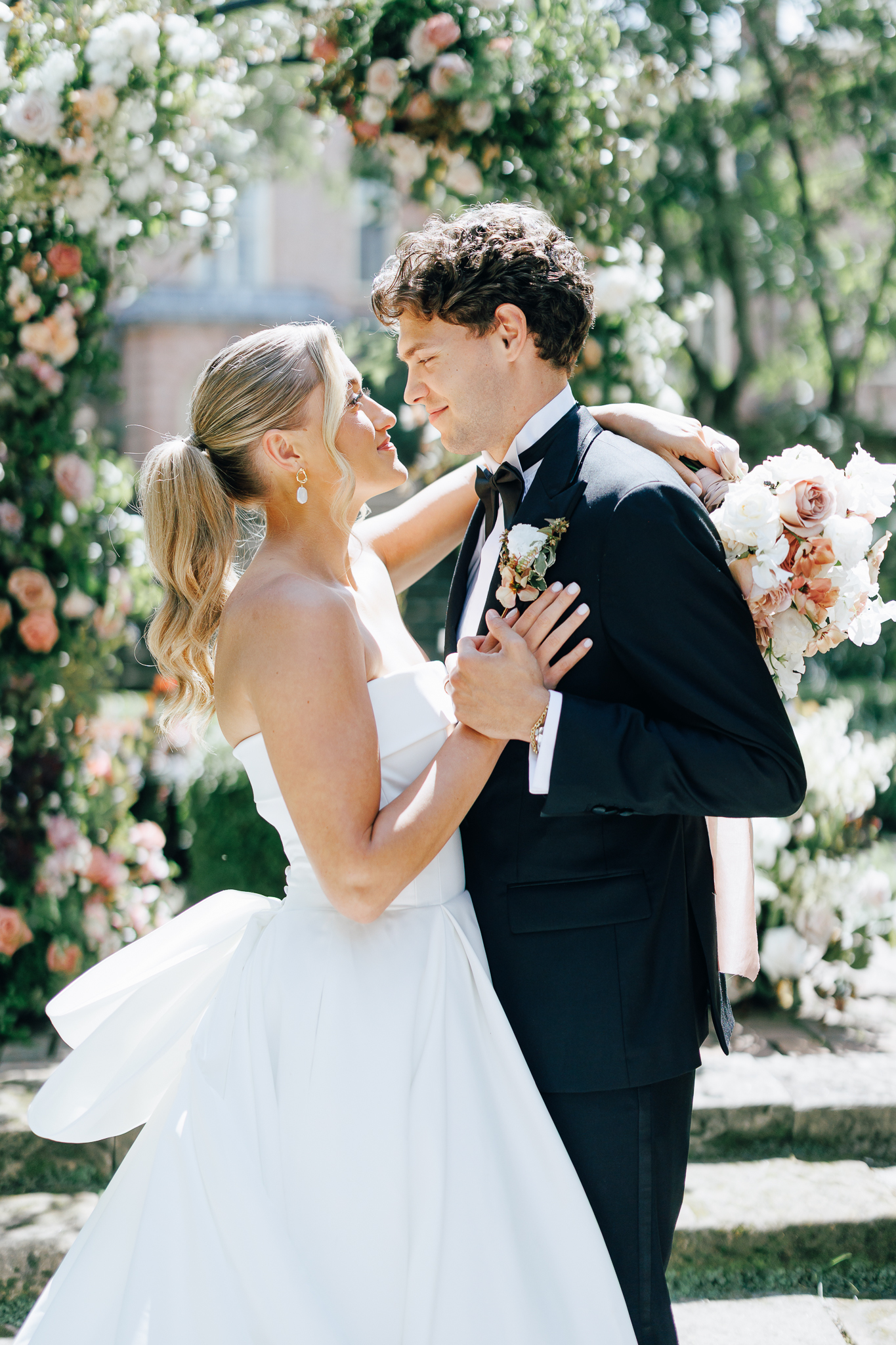 bride and groom stand under a wedding arch of pink and green florals as in luxury wedding photography